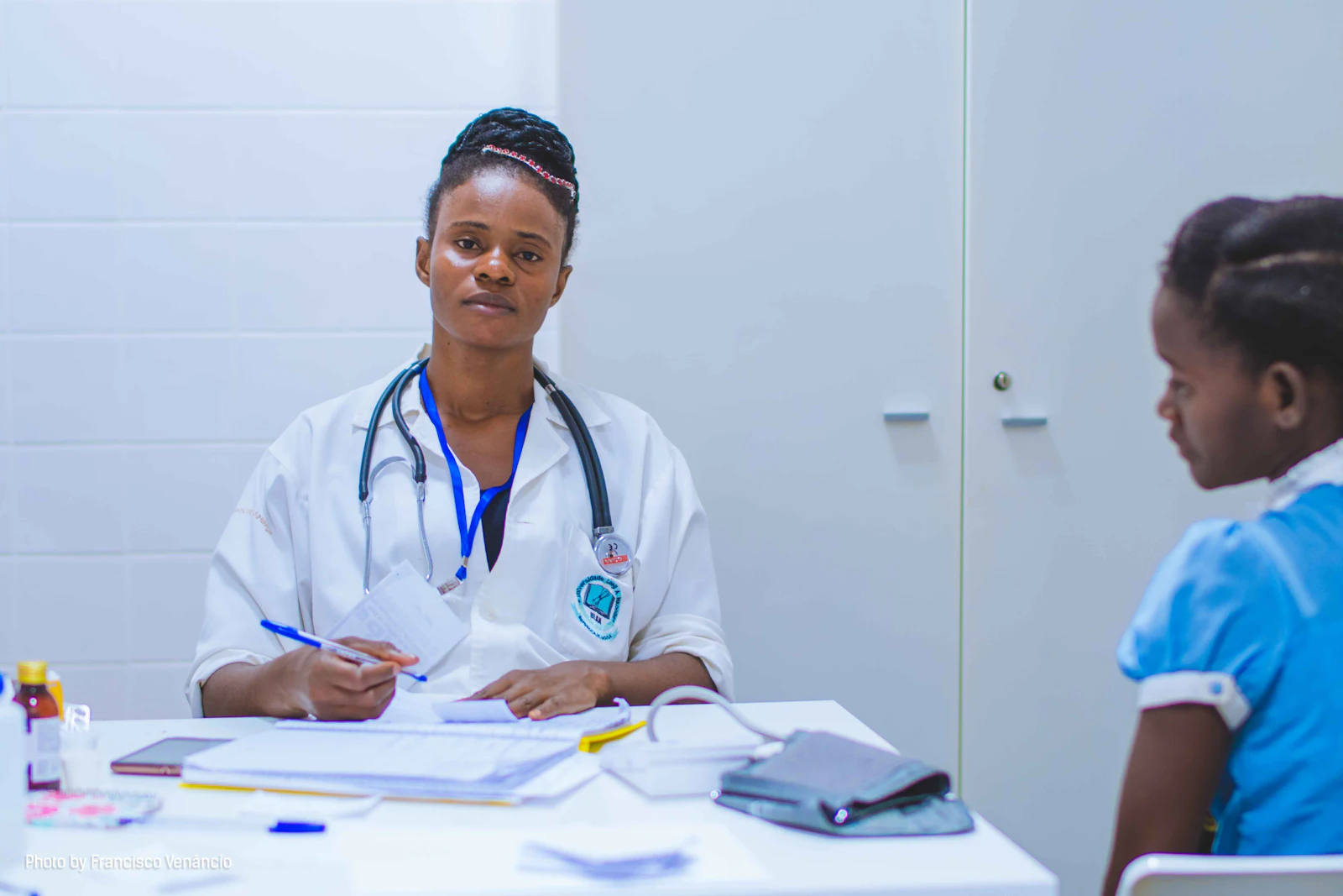 A doctor in a white coat speaking with a young patient at a consulting desk
